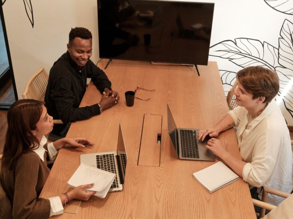 Meeting with three people. Seated around a table with a blank monitor at the end of the table.